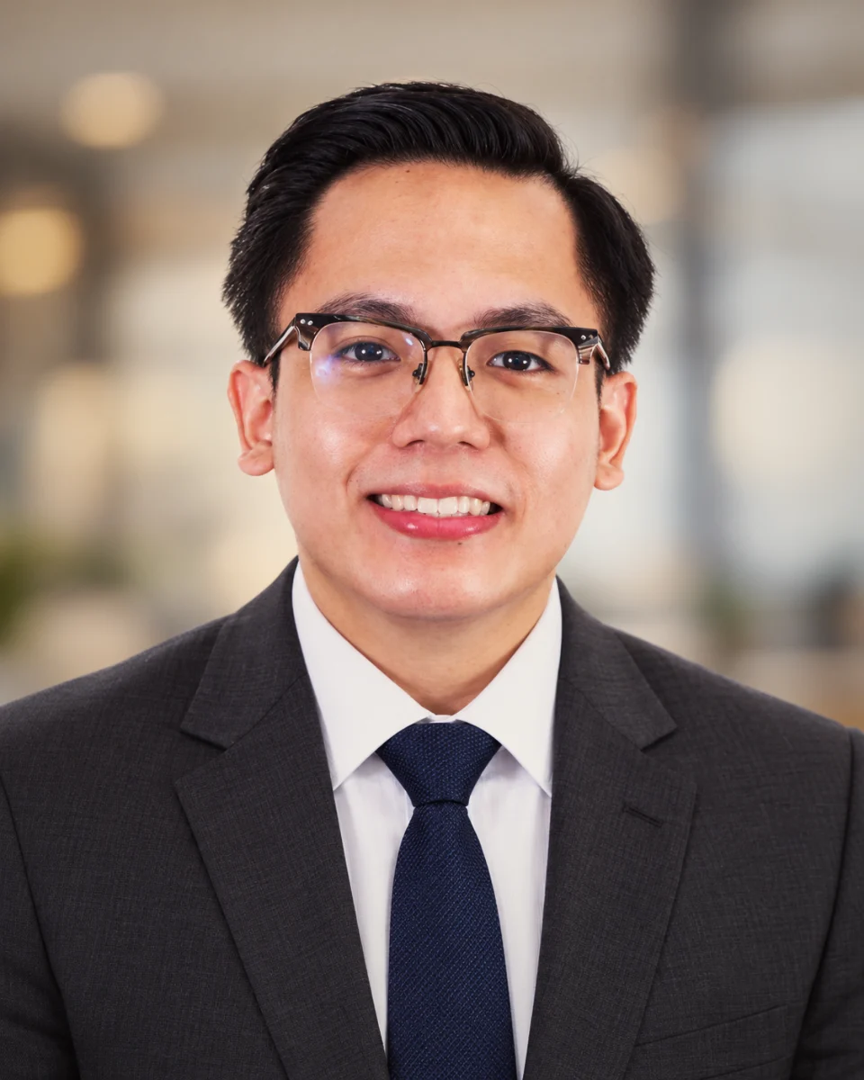 RJ Jalosjos smiling, in glasses, a charcoal suit and a navy tie.